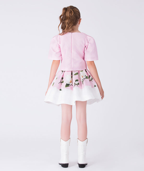 Back view of a pink floral girls occasion outfit featuring a short sleeve structured top and a matching flared skirt with contrast hem, styled for birthdays, weddings, garden parties, and special occasions, available in sizes 3–12
