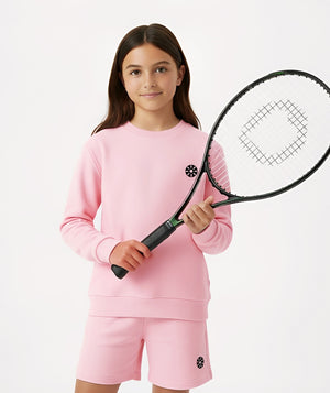 Front-facing lifestyle image of a girl holding a tennis racket while wearing a pink long sleeve sweatshirt and matching shorts, styled for sporty afternoons, active play, and everyday comfort, available in sizes 3–14
