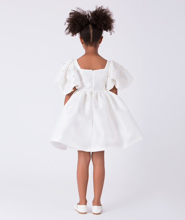 Back view of ivory girls dress featuring flared skirt and elegant puff sleeves with pearl detail.