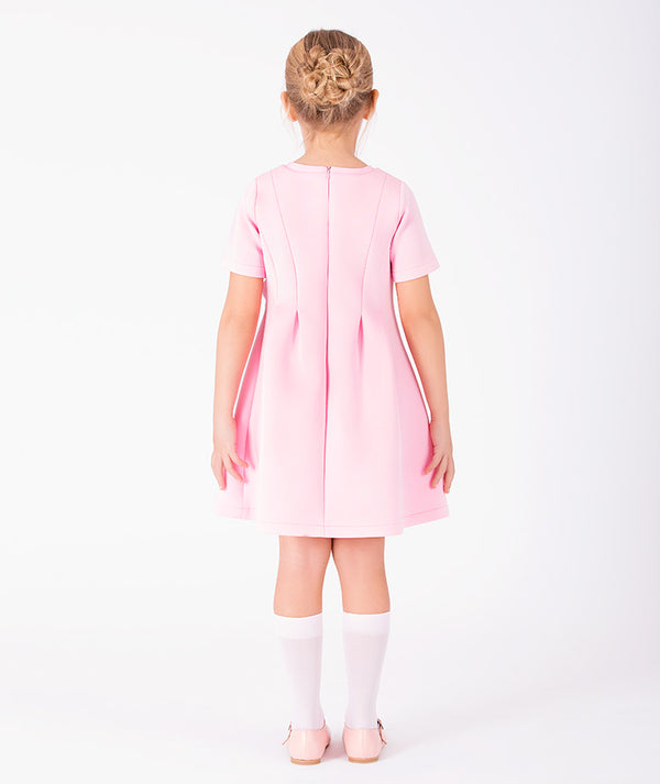 Editorial view of Rose Appliqué Girls Dress in blush pink structured fabric for girls ages 3 to 12, featuring neckline, sleeves and embellishments