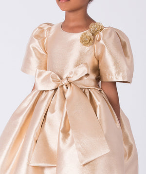 Close-up of gold satin girls dress featuring floral shoulder appliqué and oversized waist bow detail.