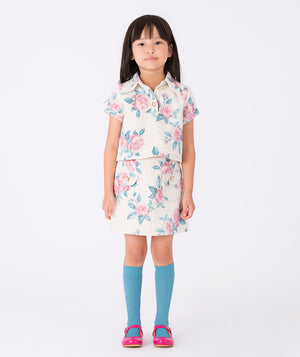 Girl wearing a short-sleeve floral tweed blouse (3–12Y) in an ivory base with pink rose prints and gold-tone buttons, ideal for birthdays, Easter, and elegant celebrations.