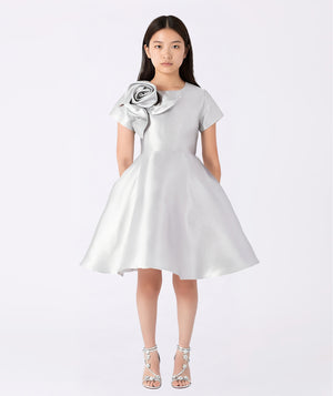 Front view of the Silver Flower Detail Event Dress by Mama Luma, showcasing a luminous silver satin finish with a dramatic floral appliqué at the shoulder. The structured yet flowing silhouette captures elegance and movement—ideal for galas, weddings, and family celebrations.