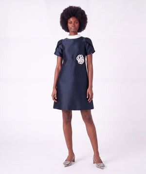 Front view of the Suva Maia Flower Women’s Dress in navy featuring an ivory high collar and sculptural flower appliqué by Mama Luma.