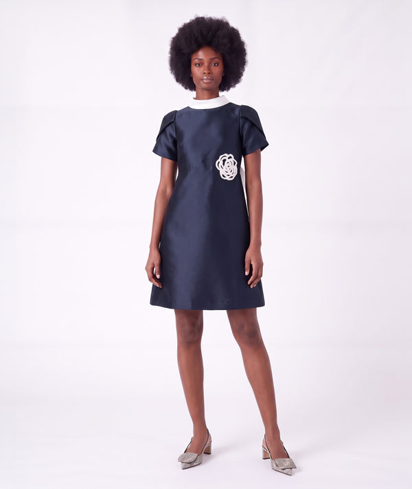 Front view of the Suva Maia Flower Women’s Dress in navy featuring an ivory high collar and sculptural flower appliqué by Mama Luma.