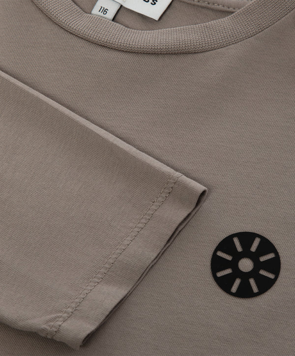 Close-up detail of a taupe girls long sleeve t-shirt highlighting the sleeve hem, neckline, soft knit texture, and minimalist chest emblem, designed for everyday wear, school outfits, and casual looks, available in sizes 3–14
