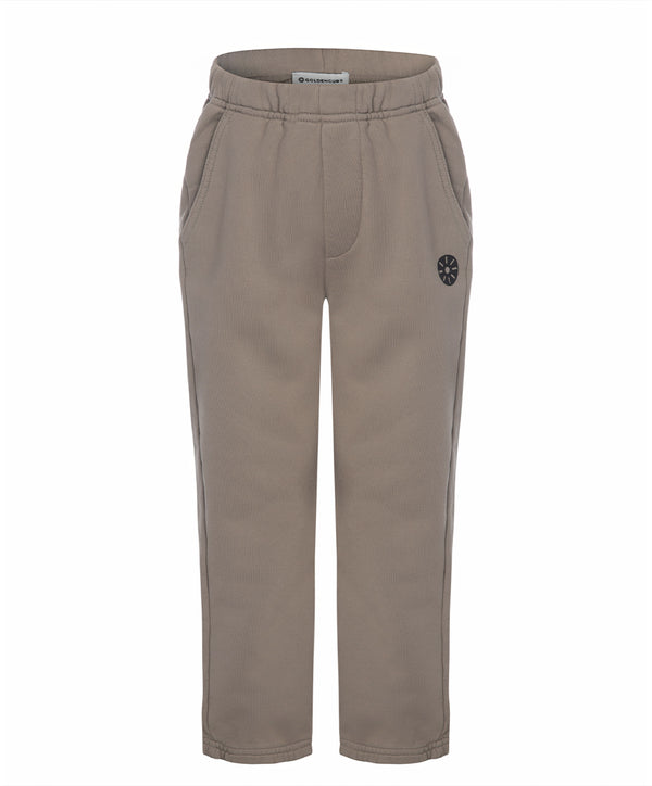 Front view of taupe girls pants with an elastic waistband, side pockets, and minimalist emblem detail, designed for everyday wear, school outfits, and casual looks, available in sizes 3–14