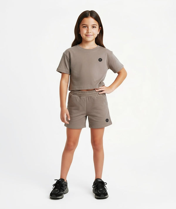 Front-facing lifestyle image of a girl wearing a taupe cropped short sleeve t-shirt with elastic-waist shorts, styled for warm-day comfort, casual movement, and easy everyday wear, available in sizes 3–14