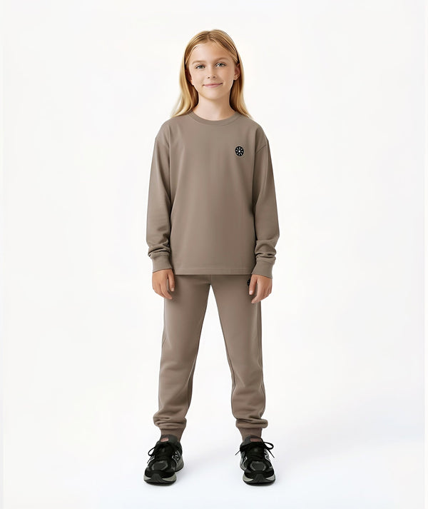 Front-facing lifestyle image of a girl wearing a taupe long sleeve sweatshirt with coordinating pants, styled for clean everyday outfits, school-ready comfort, and relaxed daily movement, available in sizes 3–14
