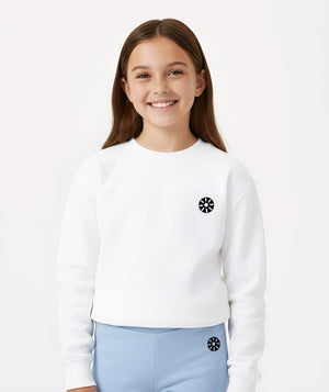 Cropped lifestyle image of a smiling girl wearing a white long sleeve sweatshirt with a minimalist chest emblem, styled for everyday comfort, school outfits, and casual layering, available in sizes 3–14