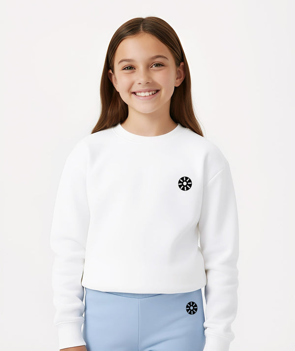 Cropped lifestyle image of a smiling girl wearing a white long sleeve sweatshirt with a minimalist chest emblem, styled for everyday comfort, school outfits, and casual layering, available in sizes 3–14