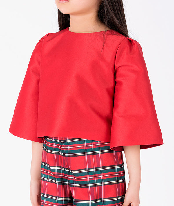 Close-up of the scarlet-red cropped top with gathered shoulders and bell sleeves, paired with multicolored plaid trousers by Mama Luma.