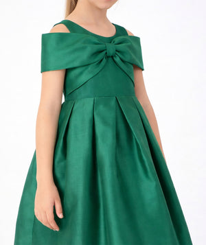 Close-up of Mama Luma Enchanting Bow Girls Holiday Dress featuring an oversized emerald-green shoulder bow and structured pleated skirt.