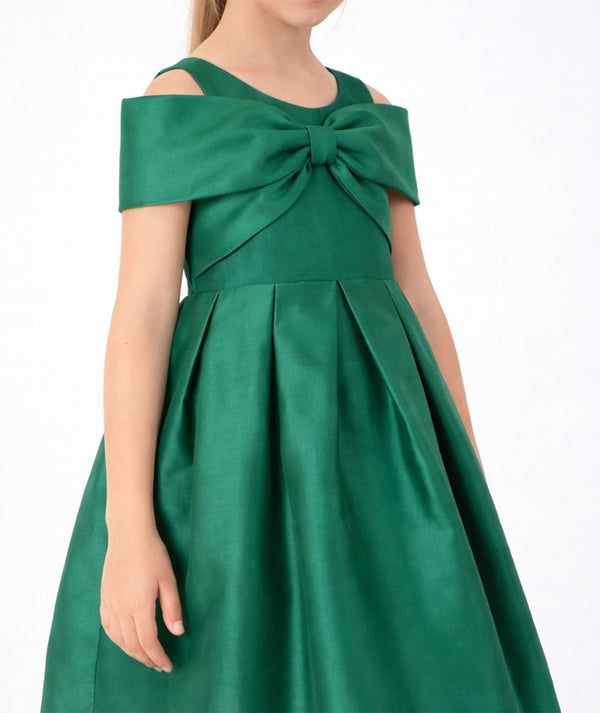 Close-up of Mama Luma Enchanting Bow Girls Holiday Dress featuring an oversized emerald-green shoulder bow and structured pleated skirt.