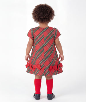 Back view of Mama Luma Tartan Baby Girl Bow Dress from the Zermatt Collection, featuring diagonal tartan checks, a concealed zipper, and red bows along the flared hem.