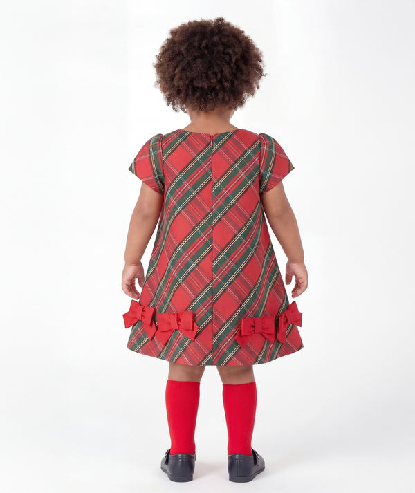 Back view of Mama Luma Tartan Baby Girl Bow Dress from the Zermatt Collection, featuring diagonal tartan checks, a concealed zipper, and red bows along the flared hem.